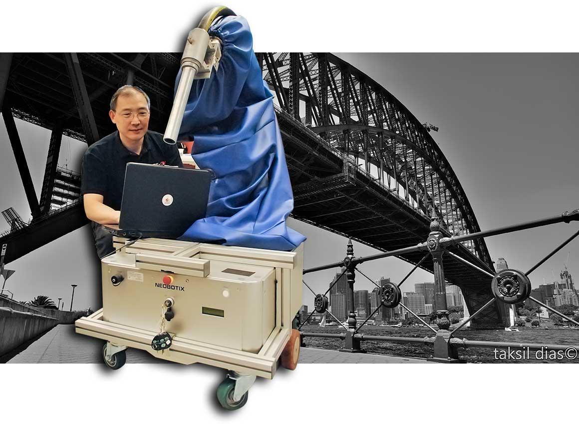 Photo of UTS Professor Kikai Liu and his grit-blasting robot, with the Sydney Harbour Bridge in the background