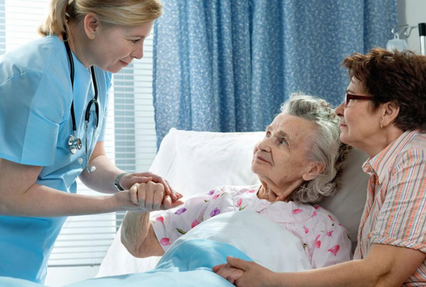 Women in palliative care holding hands with a nurse