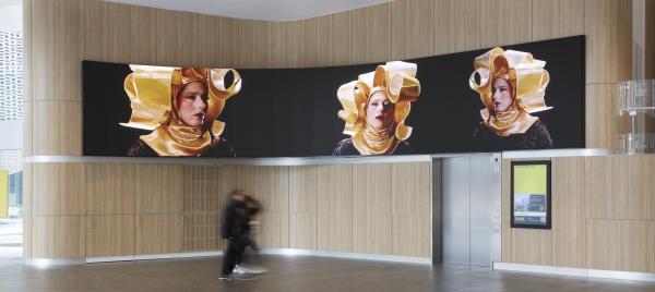 A large LED screen showing three images of people in elaborate gold headpieces