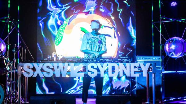 A DJ stands on stage behind a SXSW Sydney sign