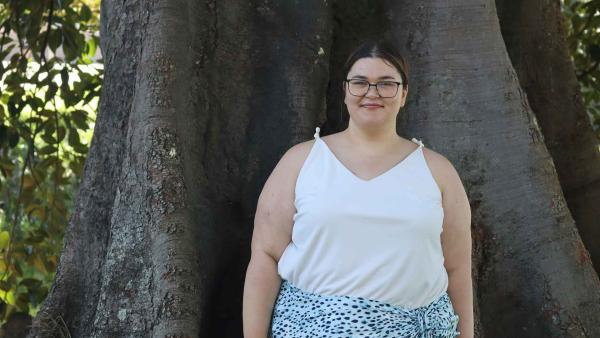 UTS master's student Rhiannon Brownbill stands outside in front of a large tree. 