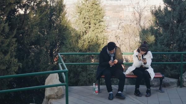 couple sitting on brown bench looking at their phones