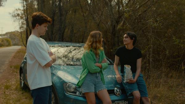 Still image from the short film The Trip which sees three characters talking around a car off the side of the road