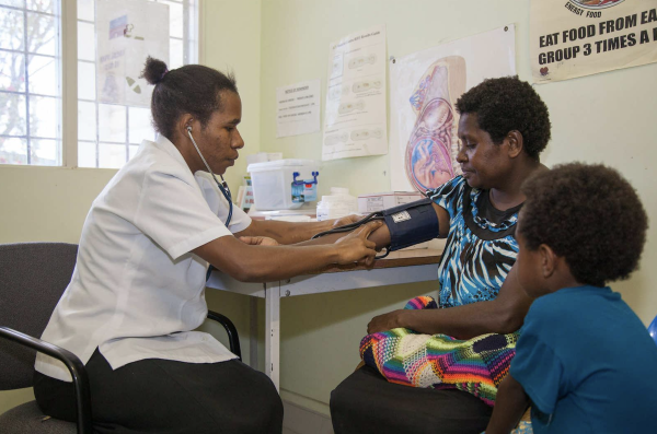Nurse checking blood pressure of woman with child seated next to her
