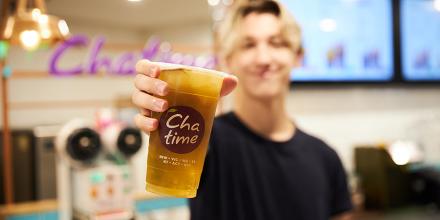 A young man holds a clear PLA cup full of iced tea