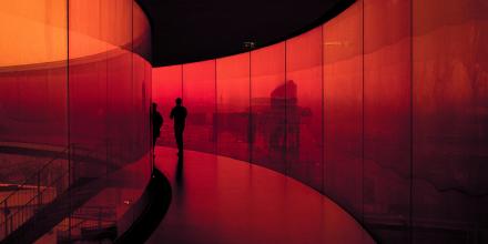 Shadow of two people walking down a curved red lit corridor