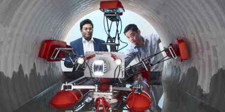 A robot with five arms in a tunnel and two researchers looking on