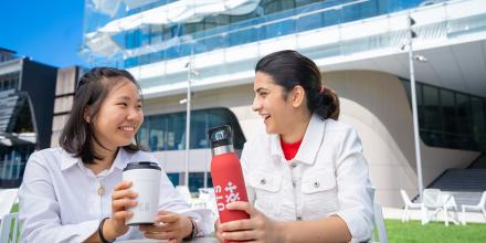Two students sitting together socialising and having a coffee and holding a red UTS water bottle