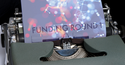 Typewriter with page with text 'Funding Round 1' shown with colourful lights and connections as a background image on the page