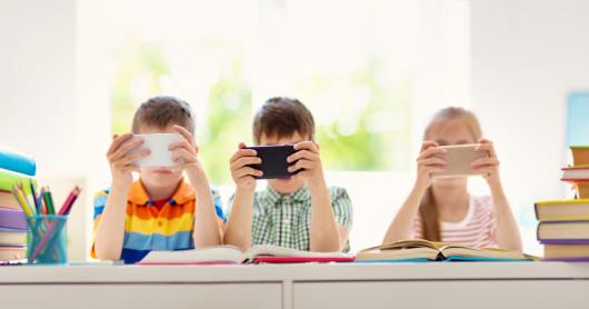 Three children playing with mobile phones in the classroom