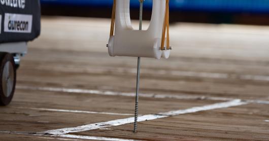 a robot arm screws a screw into a timber floor.