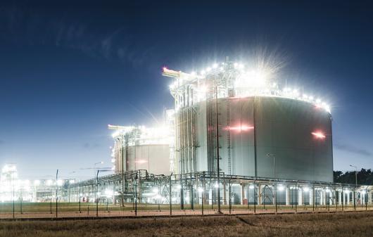A liquefied natural gas storage facility at night with two large storage tanks in the foreground