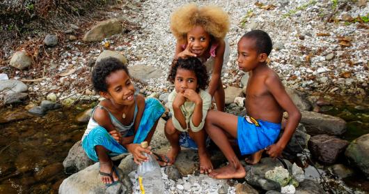 A group of kids sit on rocks by a river in Fiji.