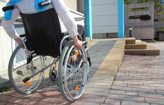 Stock image of a person in a wheelchair ascending a ramp at a private home