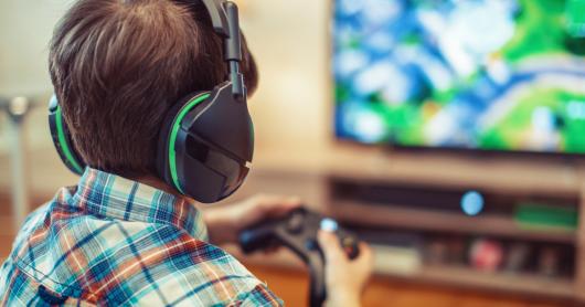 A child wears headphones and holds a remote controller to play video games.