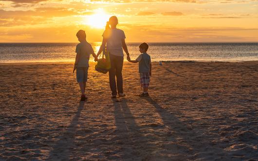 Stock picture of a mother and two children on a beach at sunset