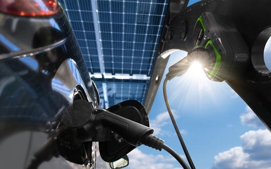 Stock picture of an electric car being charged with solar panels above