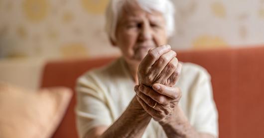 An older person holds one hand to their wrist, face expressing pain.