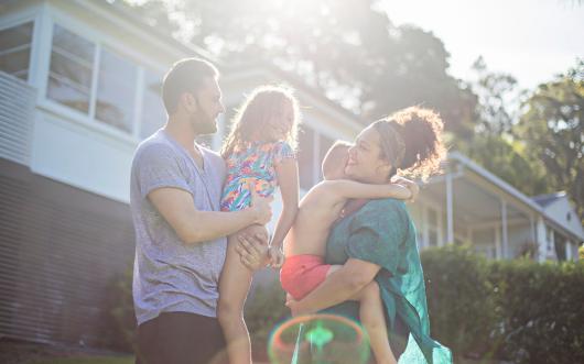 Stock image of a First Nations family outside a suburban home