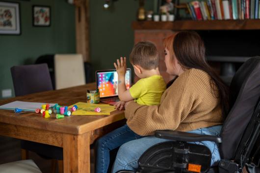 Woman in wheelchair sitting at table with son, looking at laptop