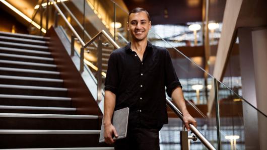 SQ PhD Student Mauro Morales standing on a staircase in UTS's Building 11, smiling and holding his laptop.