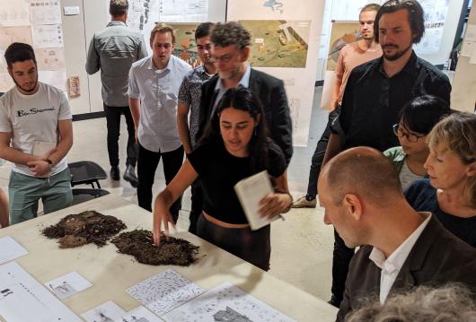 Group of people chatting around a desk covered with landscape samples and paperwork 