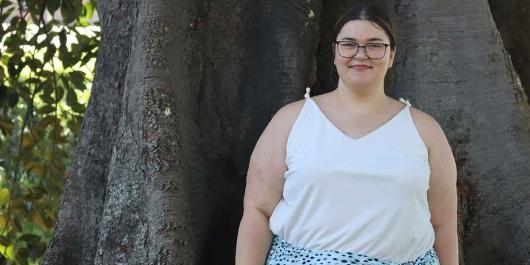 UTS master's student Rhiannon Brownbill stands outside in front of a large tree.