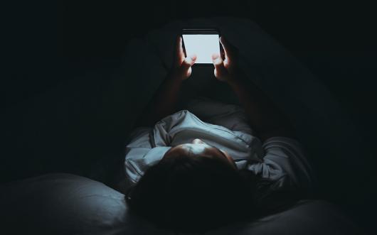 A woman looking at a mobile phone in bed. Picture: Adobe Stock