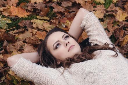 A young woman lying down in a pile of Autumn leaves 