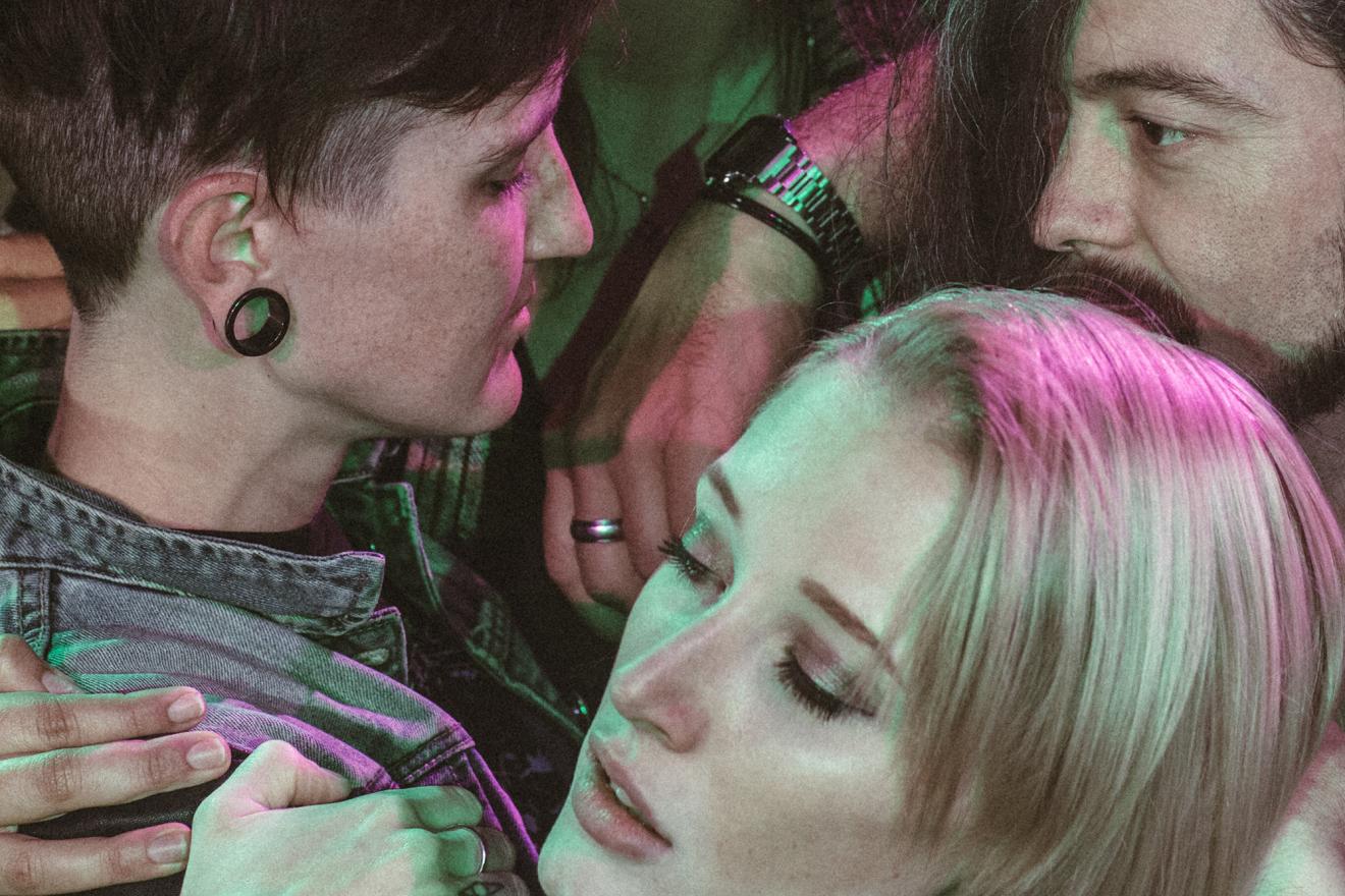 Close-up of faces in a mosh-pit, reflecting by purple and green lighting