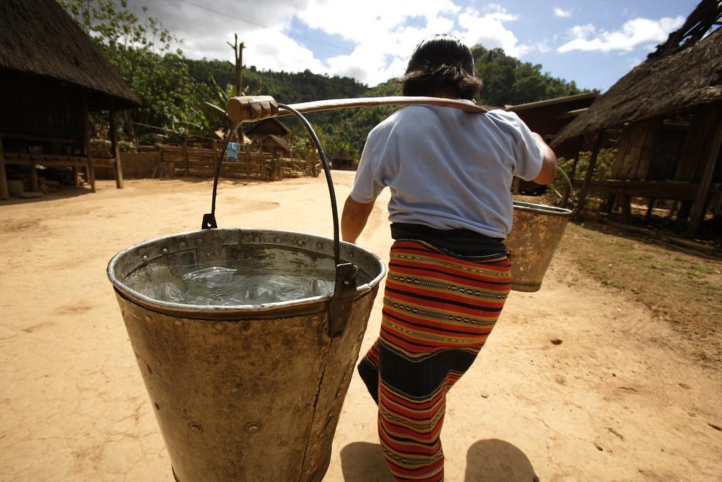 A woman in a rural village carrying buckets of water