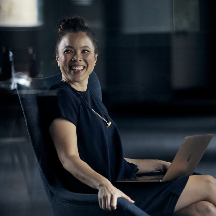A woman in business attire working on a laptop and smiling