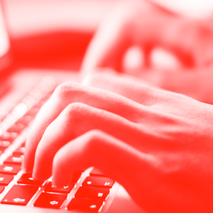 Duotone red and white close-up image of a persons hands typing on a laptop keyboard