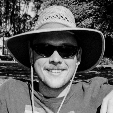 Black and white image of young man wearing hat and sunglasses and smiling at camera