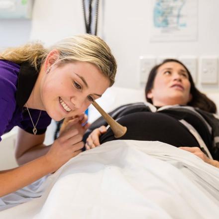 Midwifery student listening to a baby’s heartbeat through a Pinard stethoscope