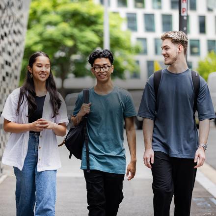 Three students walking and smiling on campus at UTS