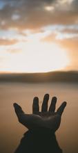 Hand in front of landscape sunset