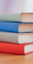 Four books with red, grey, blue, green covers stacked on top of each other