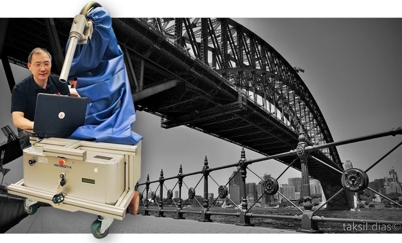 Photo of UTS Professor Dikai Liu and his grit-blasting robot, with the Sydney Harbour Bridge in the background