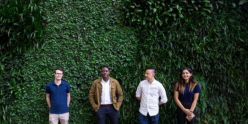 Four students standing in front a green wall of plants