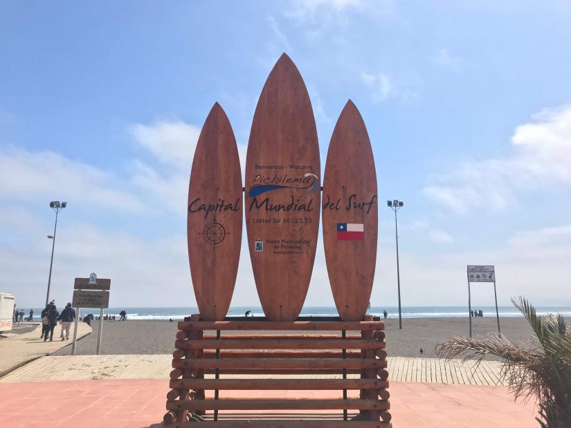three board signpost reading 'Capital Mundial del Surf' in front of the coastline in Chile