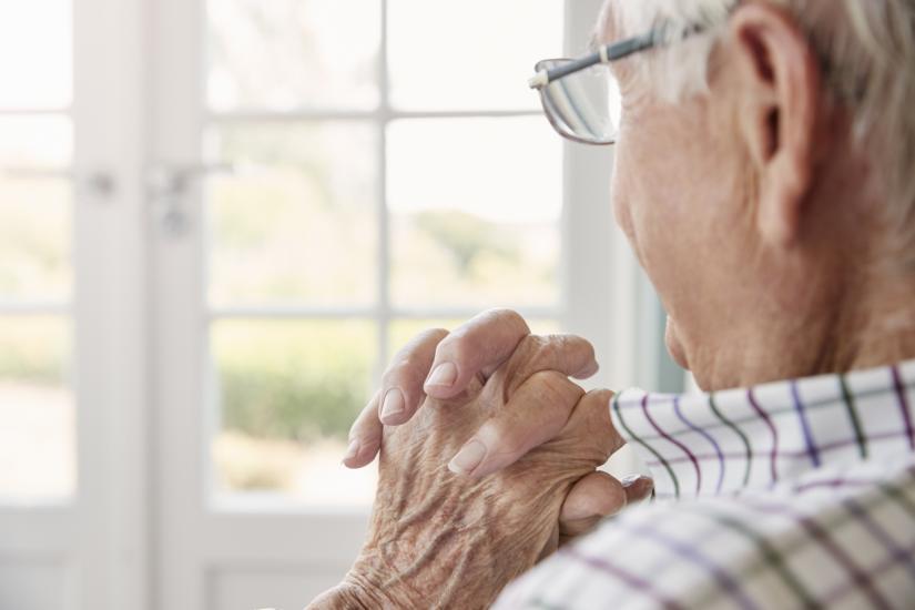 elderly man with hands crossed looking out window