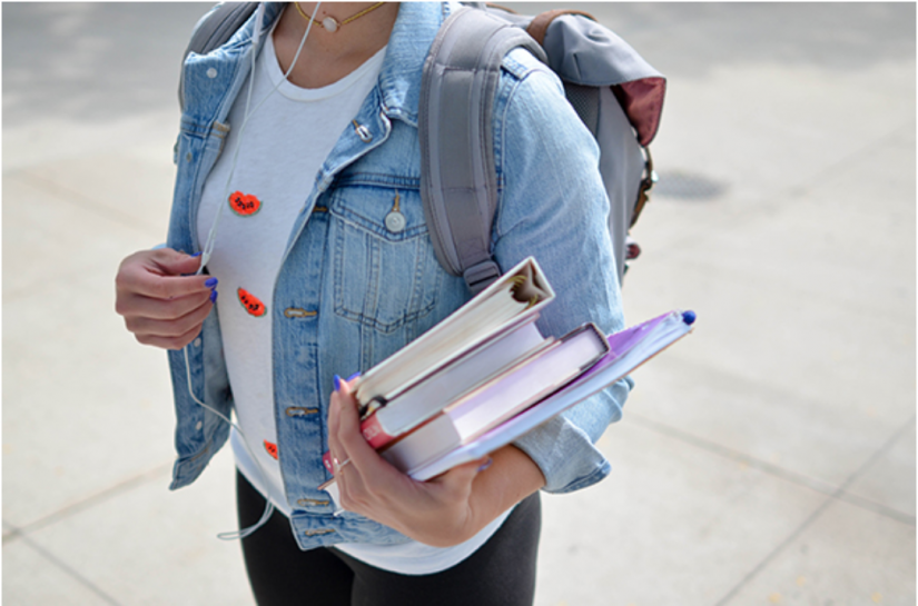Mid shot of a person in a denim jacket, with a backpack and books
