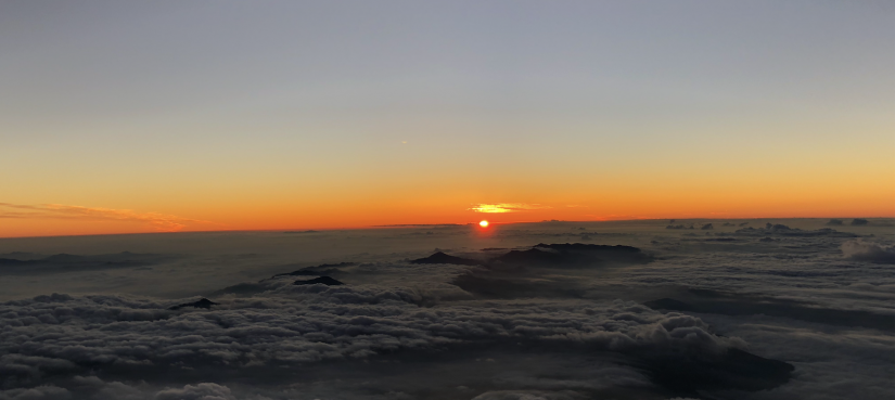 The sun rising above the clouds on top of a mountain