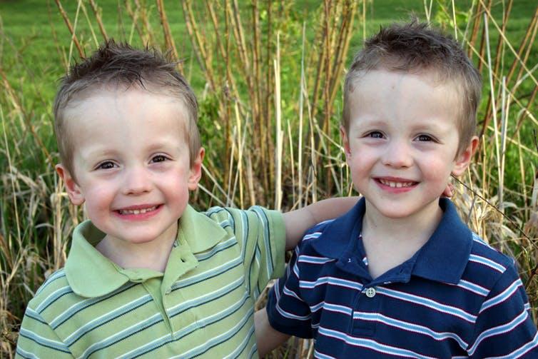 Identical twin boys smiling with arms around each other