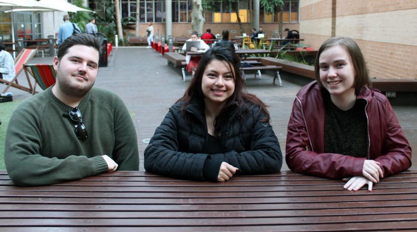Oliver, Aarya and Remi-Rose sitting at a wooden table smiling at the camera