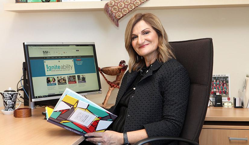 Violet Roumeliotis sitting whilst holding a book with a computer screen on in the background