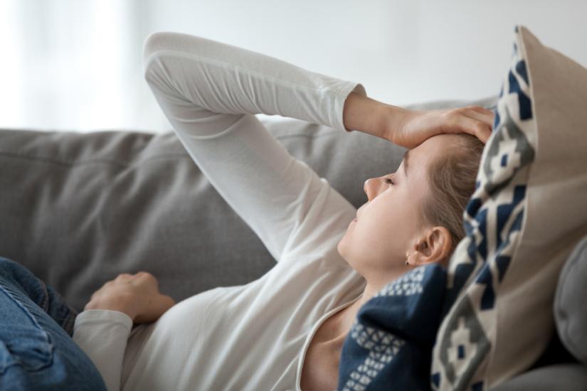 Tired woman lying on couch with her hand to her head