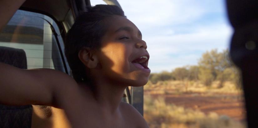 A young Indigenous boy leaning out of a car window 