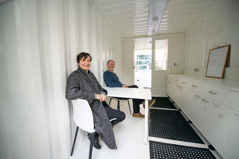 a woman and man sit in a white interior of a retrofitted shipping container